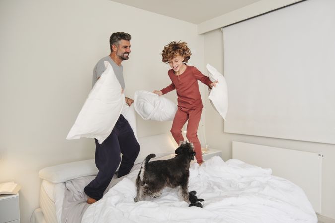 Smiling man and boy playing with dog on bed