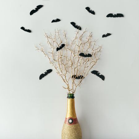 Golden champagne bottle with bats silhouettes on light background