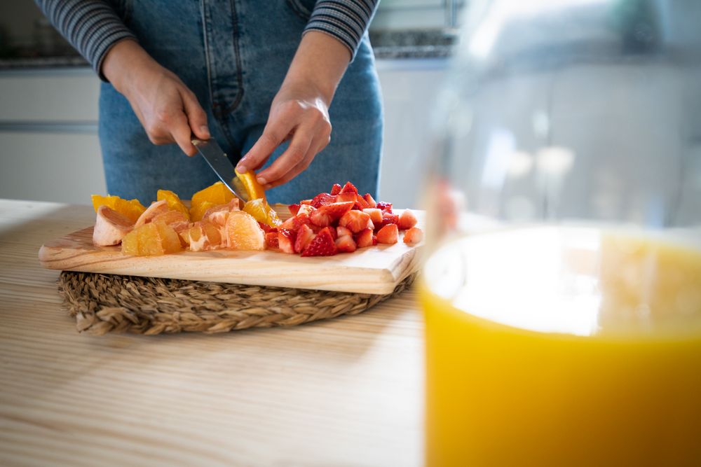 Crop woman cutting fruits for smoothie
