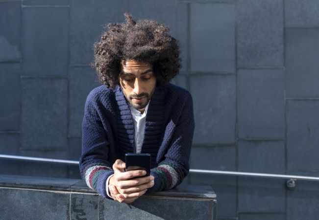 Black man in cardigan leaning forward outdoors on sunny day