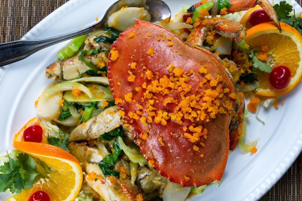 Whole cooked Dungeness crab with cheese and veggies on serving plate ready to eat