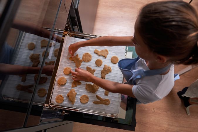 Girl in blue apron putting cookies into oven