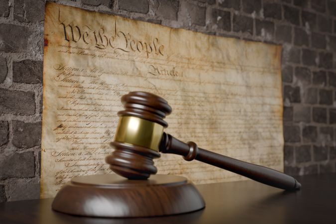 United States Constitution On Wall with Gavel Resting on Table in Front.