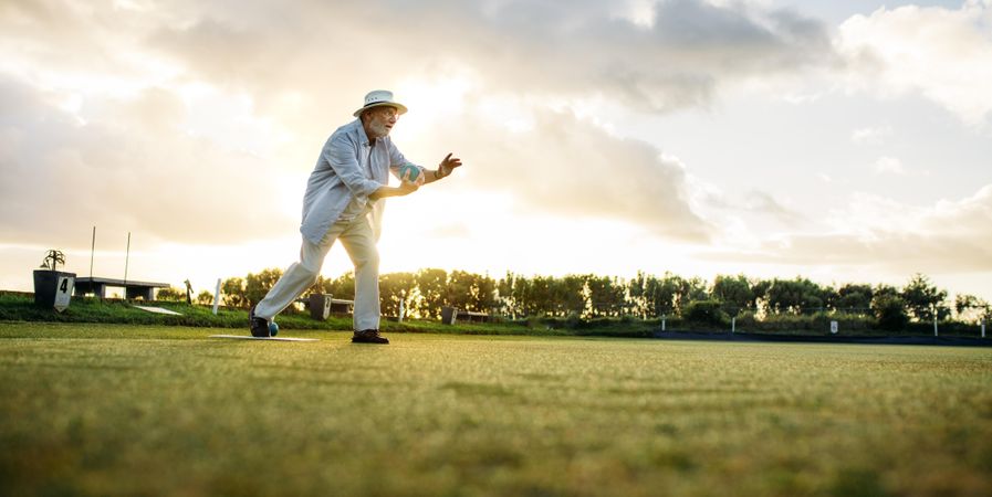 Older gentleman in hat in position to throw a boules in a lawn