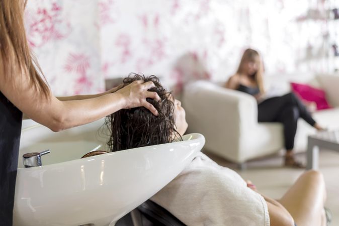 Woman having her hair shampooed in salon with another customer waiting