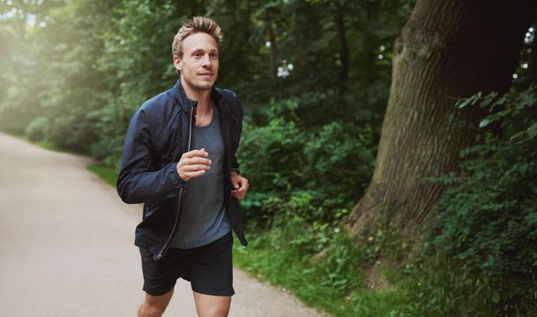 Athletic man in sporty vest & windbreaker jogging outdoors