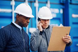 Two serious men in hard hats one on the phone