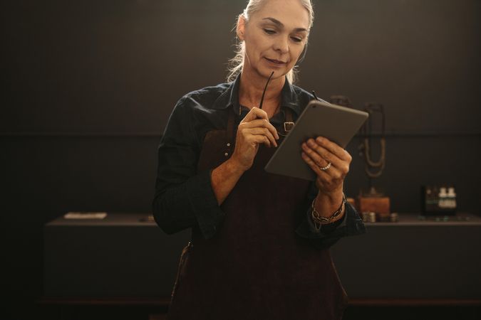 Portrait of mature woman jewelry designer using digital tablet in workshop