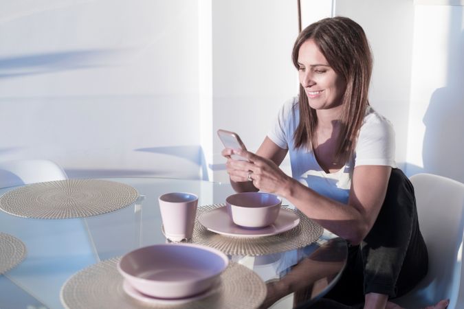 Woman sitting at sunny table checking phone in front of cereal bowl