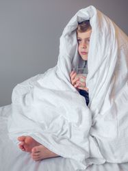 Little boy wrapped in blanket on bed