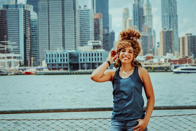 Black woman happy with her hand to her hair, other hand in pocket with New York in background