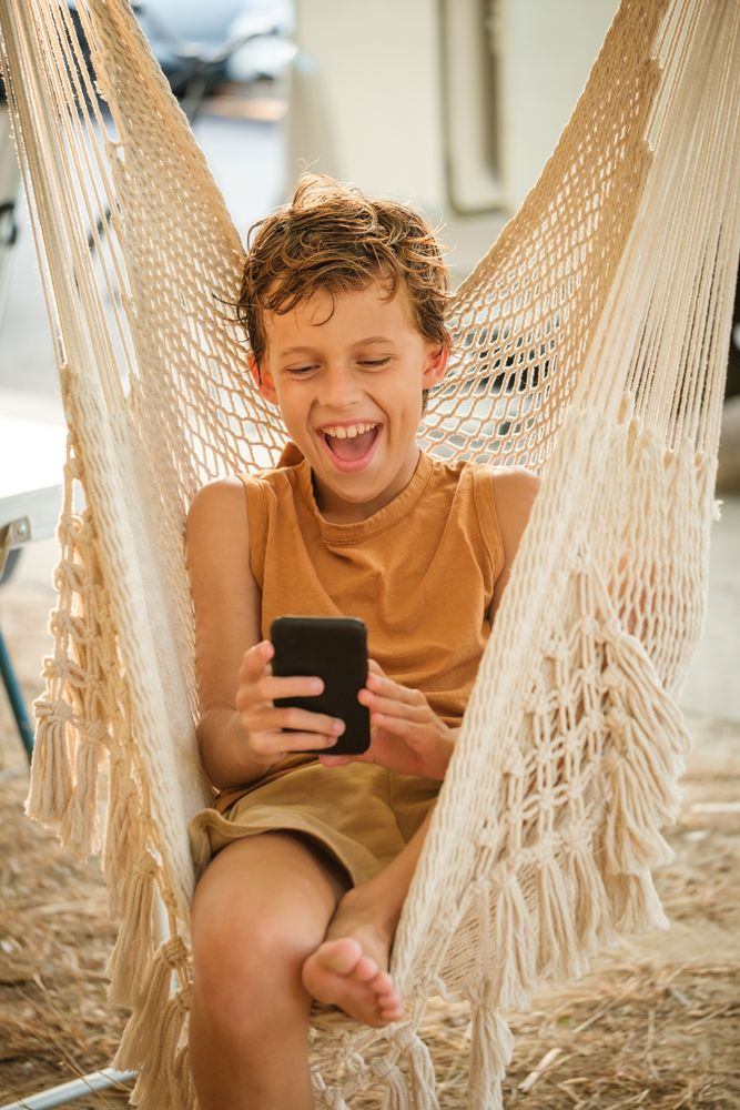 Boy with smartphone laughing at joke in hammock