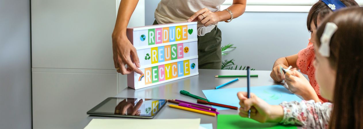 Teacher explaining to students a ecologic process using lightbox with text reduce, reuse, recycle