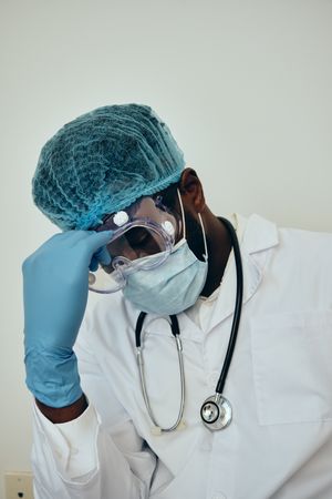 Disappointed Black male doctor in ppe gear resting his forehead on his hand
