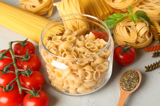 Composition with pasta, tomatoes and spices on bright background, space for text