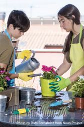 Two teenagers wearing a gardener apron watering plants on the terrace beXNvE
