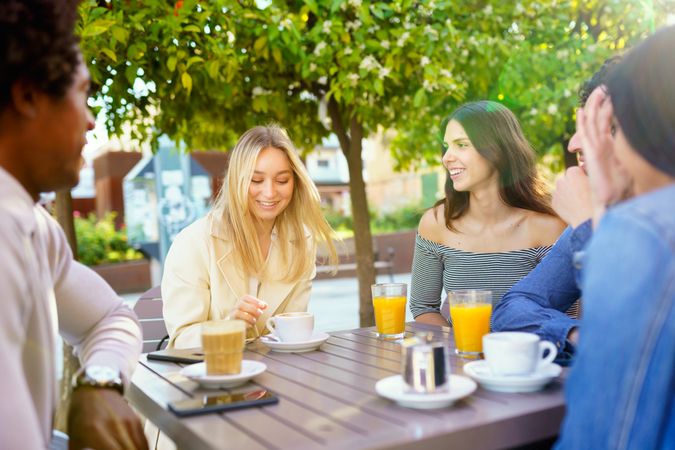 Multi-ethnic group of friends having a conversation over coffee and juice at outside table