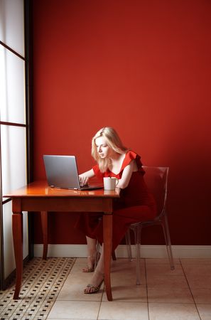 Young adult woman sitting at the table and working on laptop