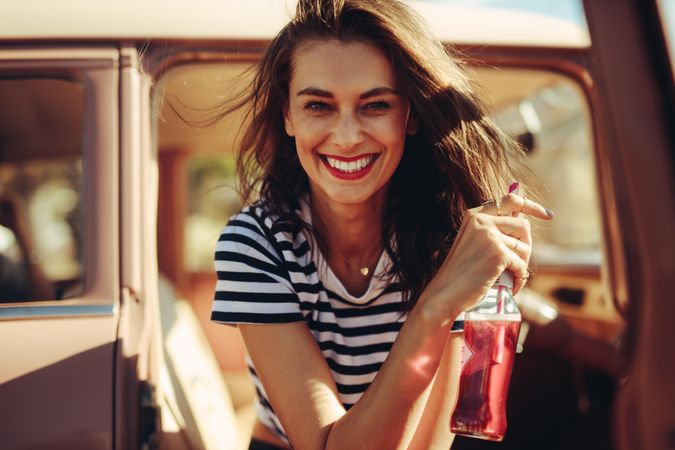 Young female with drink on a road trip while smiling at camera