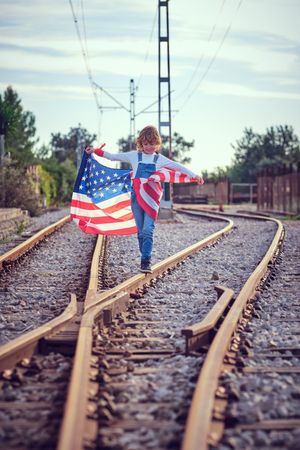 Delightful child having stroll on rails with flag of America