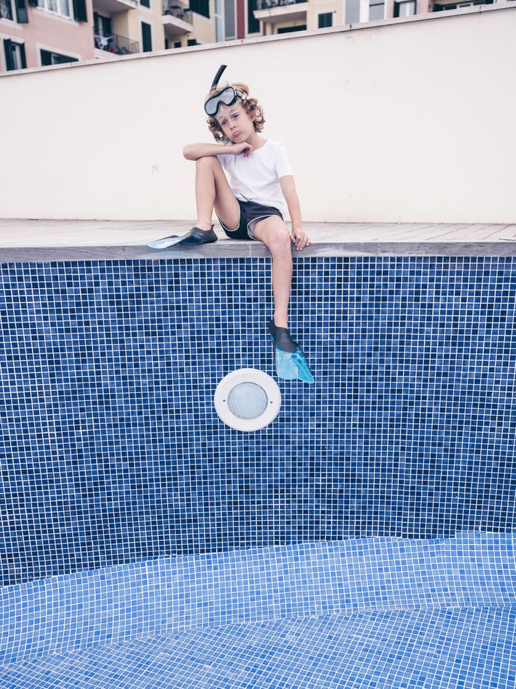 Puzzled boy in diving mask and flippers over empty pool