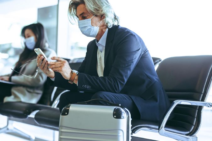 Businessman sitting on chair at airport and using mobile phone