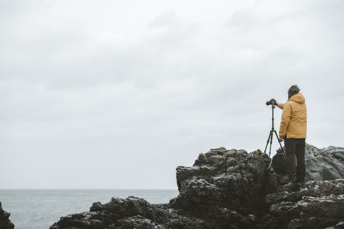 Man standing on rock and taking picture of sea