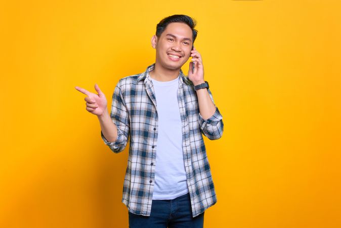 Happy Asian male talking on phone in studio shoot while pointing to the side