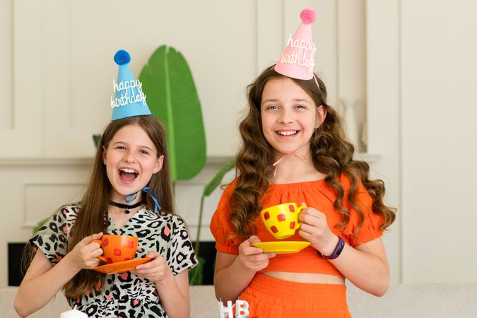 Two girls in birthday hats laughing and holding cups
