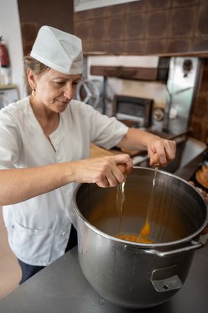 Baker woman adding eggs to a big industrial pan to prepare cupcakes