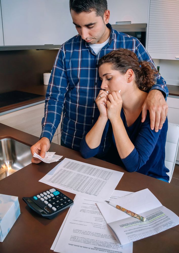 Couple supporting each other as they work through their bills together in the kitchen, vertical