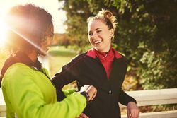 Two women smiling in windbreakers in a sunny park