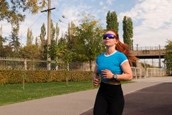 Woman jogging in park, wearing sunglasses and sportswear.