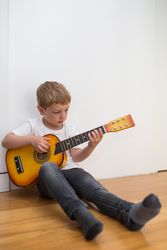 Young blonde boy playing toy guitar