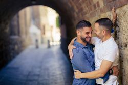 Two men smiling together in an embrace under a city bridge