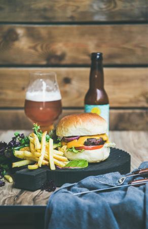 Classic hamburger with fries and beer bottle at wooden restaurant table