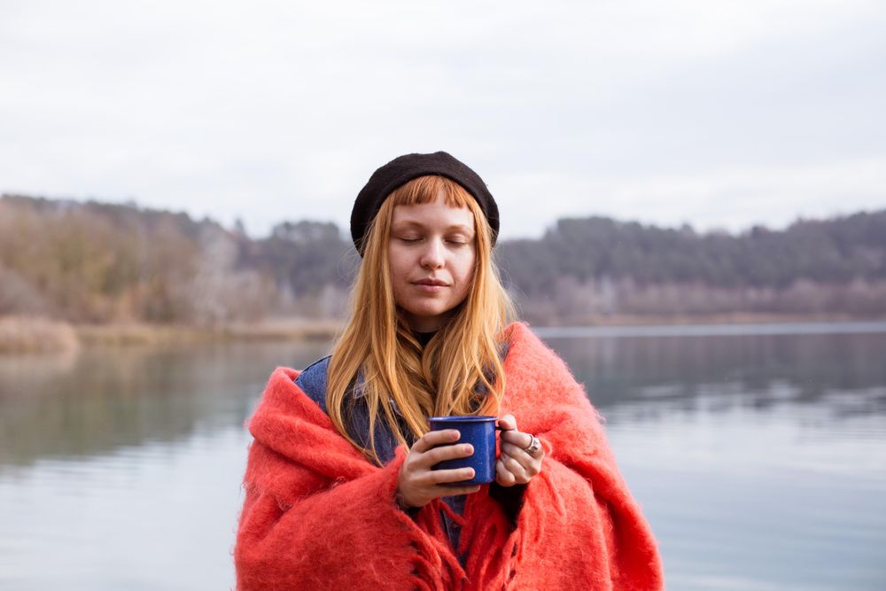 Woman outside with her eyes closed and a mug of coffee or tea