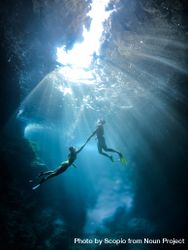 Underwater shot of man and woman diving in water and holding hands bGBvV4