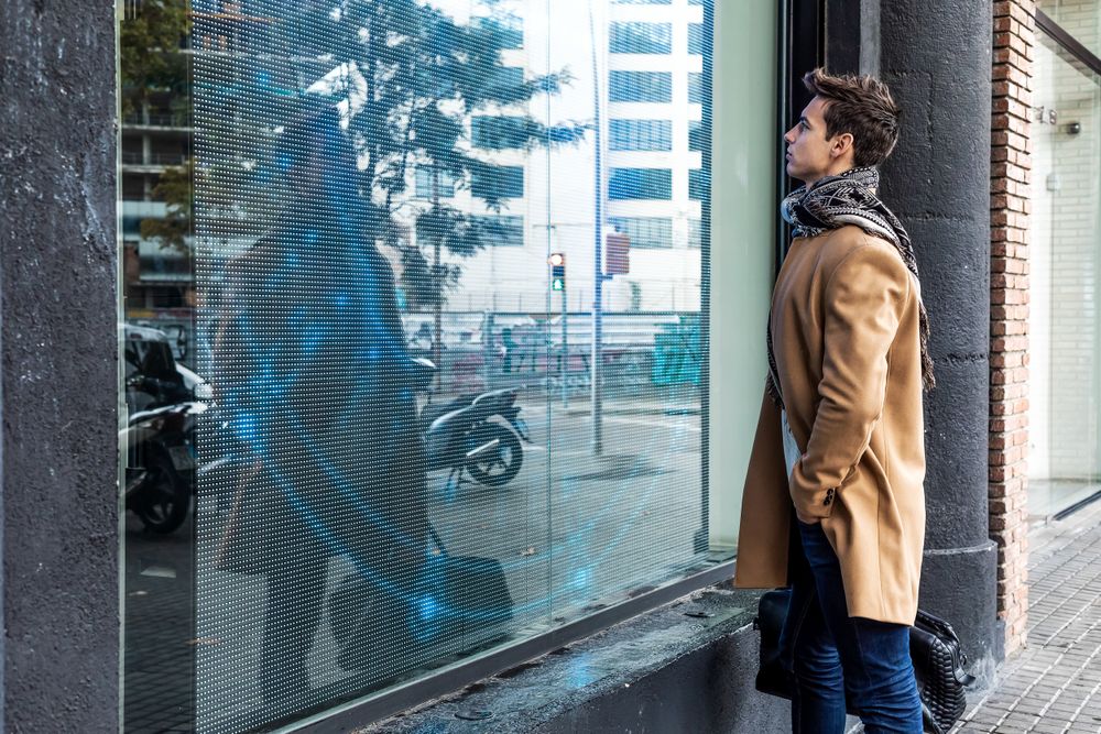Man wearing camel coat and scarf and window-shopping