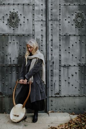 Pensive charming woman holding lyre at metal gates