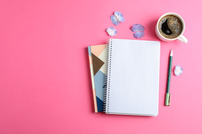 Cup of coffee with petals of flower, copybooks and pen on color background, top view