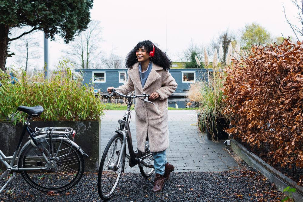Cheerful Black woman in headphones with bicycle