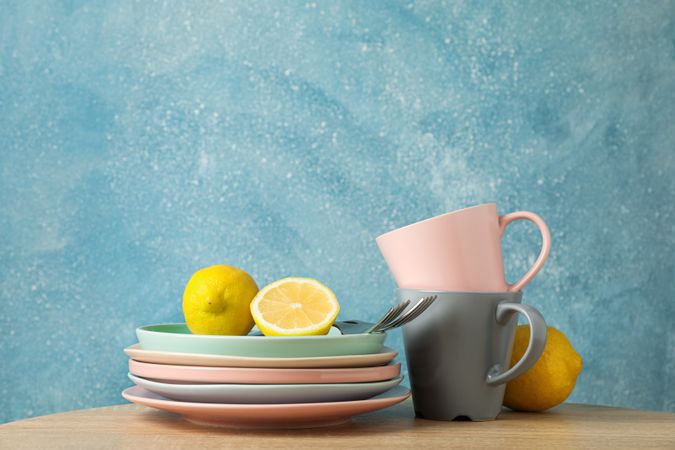 Plates and cups with lemons stacked on wooden table, space for text