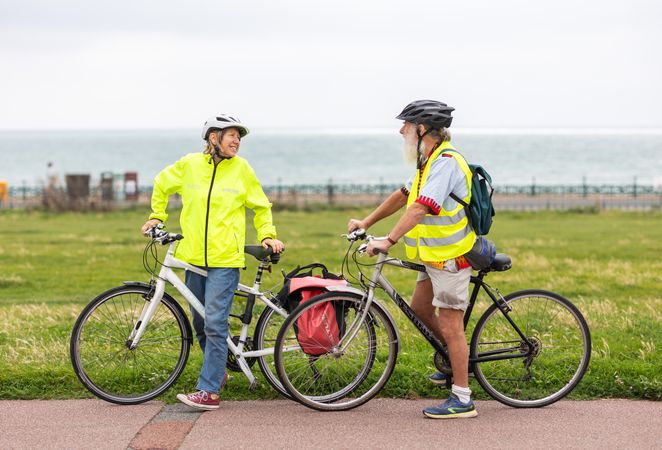 Two older people standing and talking with bikes by the coast