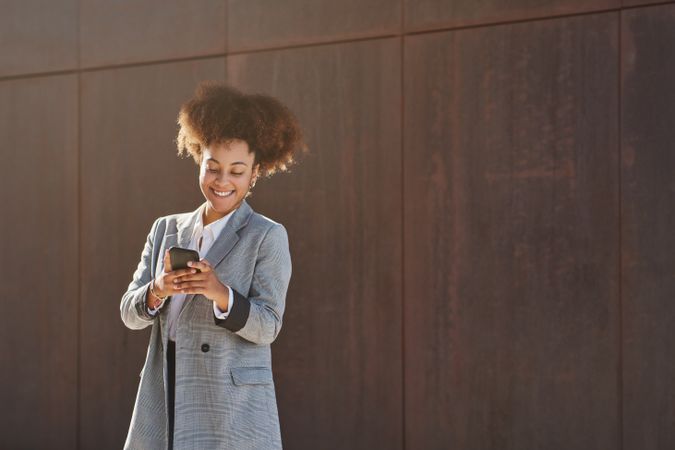 Smiling Black woman in formal clothes using smartphone
