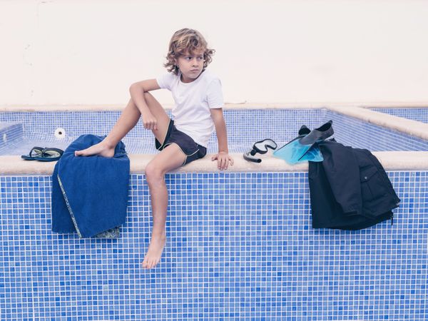 Blond boy with swimming equipment near pool