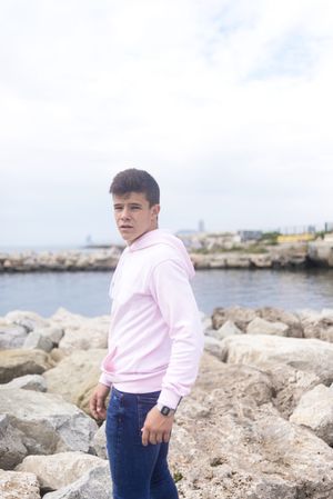 Young male teenager standing on rocky breakwater and looking at camera