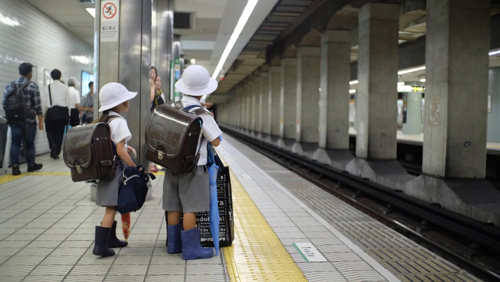 Two children with light hast and backpacks waiting at train station in Japan