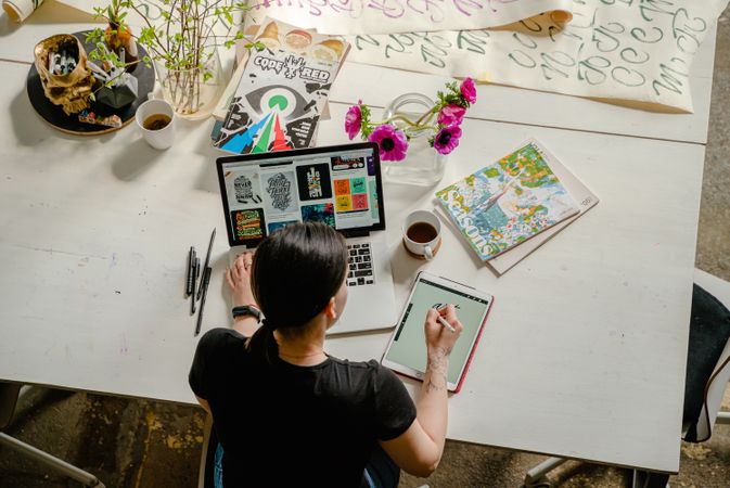 Top view of woman drawing on her tablet computer on her desk