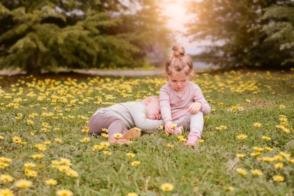 Girl and a baby sitting in yellow flower field